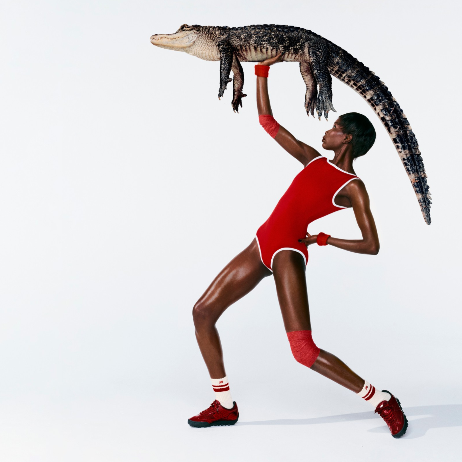A woman in front of a white background wearing Gator Run shoes while holding an alligator. 